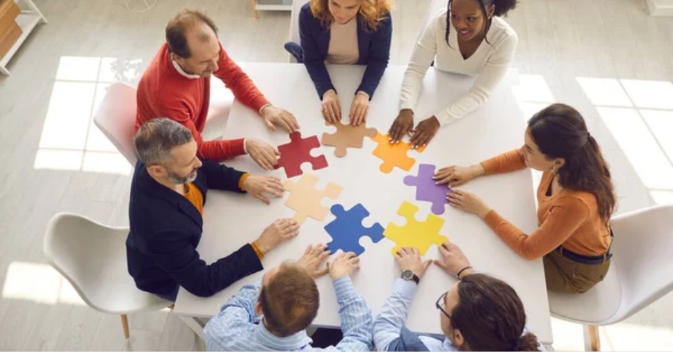 Equipe unindo peças coloridas de quebra-cabeça em mesa de gestão de projetos empresariais.