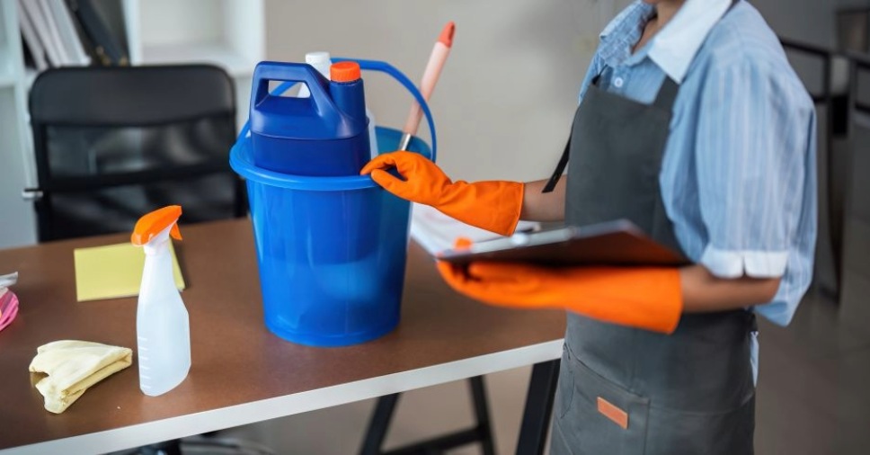 Profissional com luvas e prancheta organiza materiais no planeamento da limpeza profissional.